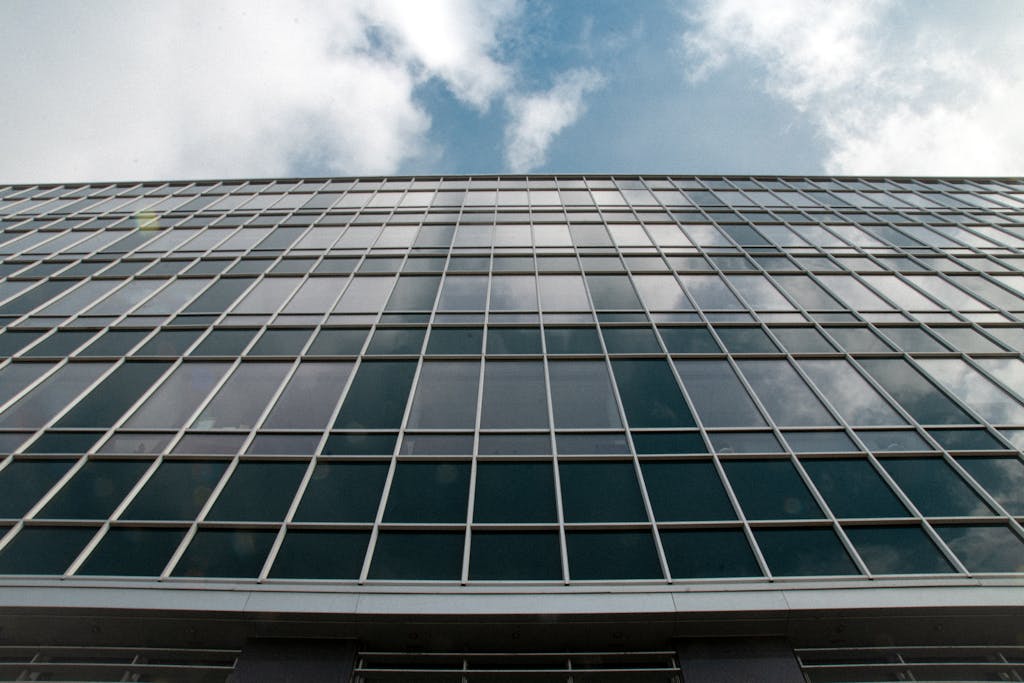 High-rise building facade with glass windows reflecting sky and clouds in an urban setting.